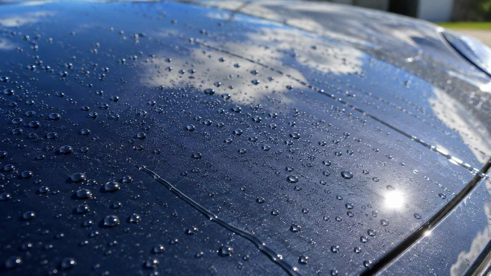 Detalhe de capô de carro escuro com gotas de água escorrendo após aplicação de proteção de pintura